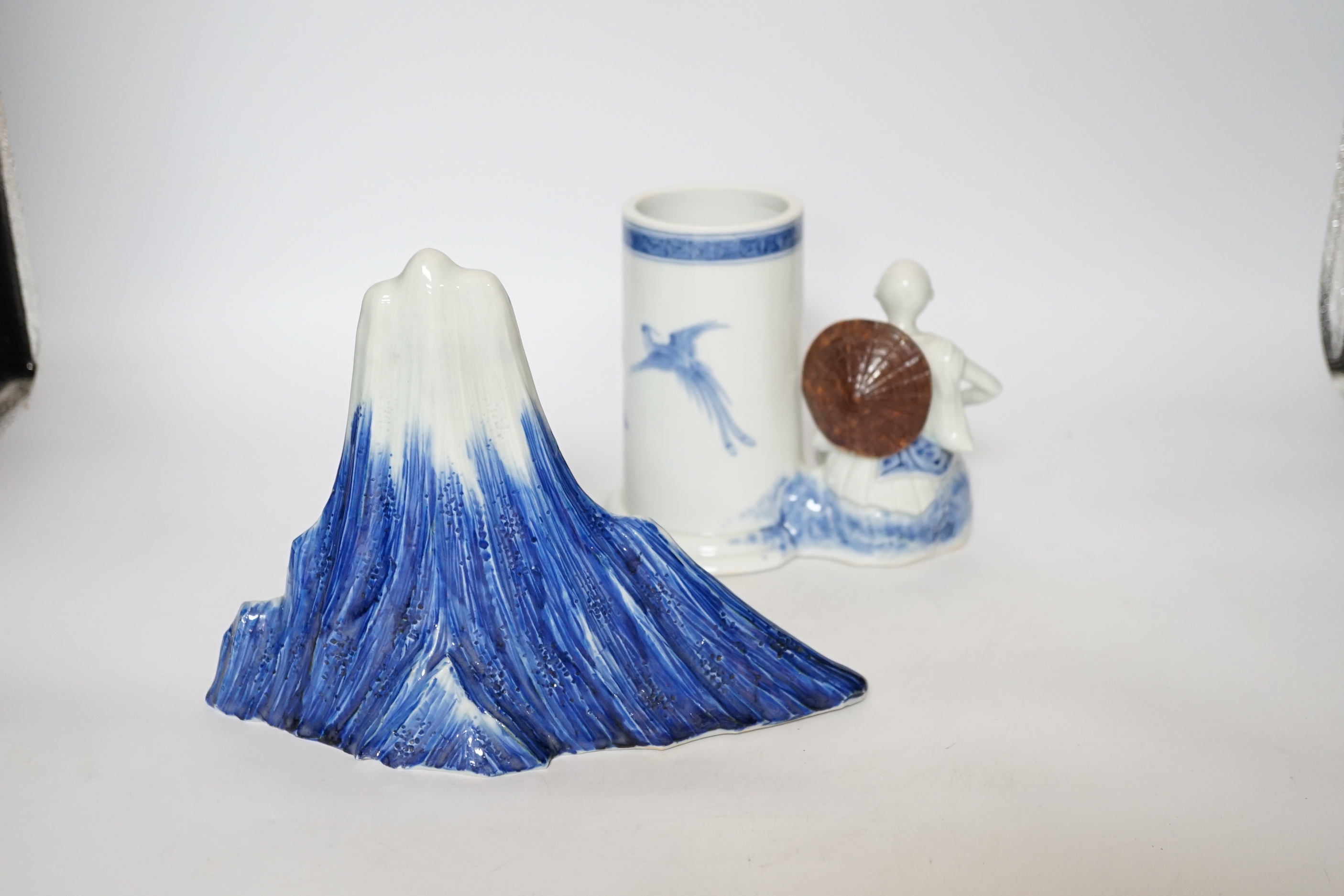 An early 19th century Japanese Hirado blue and white model of a monk seated by Mount Fuji, and a similar brush pot modelled with a fisherman seated by the cylindrical vessel, largest 17cm high (2)